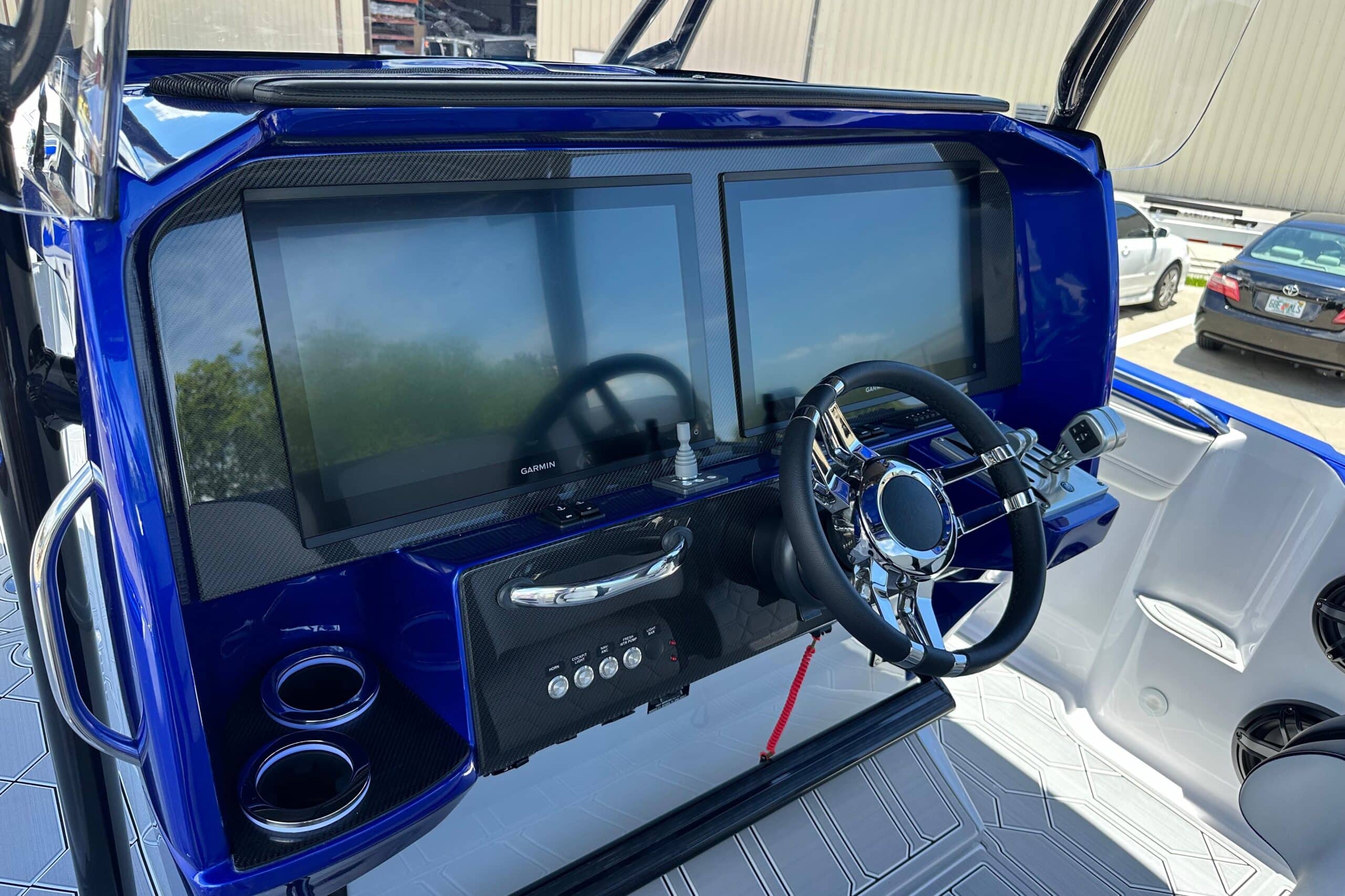 Offshore performance boat helm featuring dual Garmin navigation displays, carbon fiber dash, and stainless steering wheel
